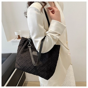 Detail of black textured tote bag featuring a branded oval plaque and long shoulder strap