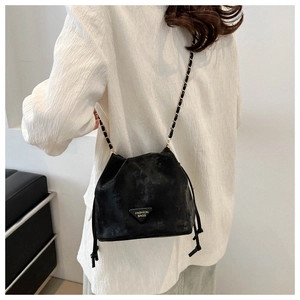 Detail der schwarzen Wildleder-Beuteltasche mit Metalllogo und Ketten-Schultergurt