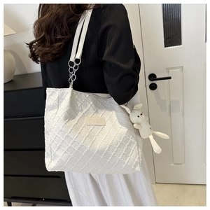 Detail of white quilted tote bag with fringe edges, chain strap and plush rabbit charm