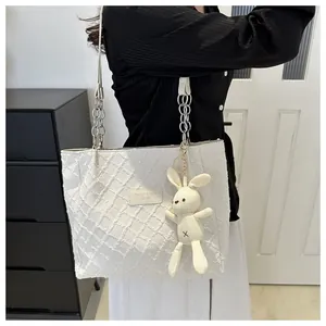 Detail of off-white tote bag with diamond texture, chain strap, and cute plush bunny charm