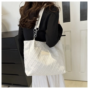 Detail of white woven tote bag with square leather patch and metal chain strap