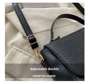 Détail du cuir gaufré crocodile et de la boucle en métal doré sur un sac noir élégant