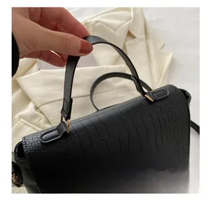 Détail d'un sac à main noir à motif crocodile avec fermoir doré et poignée élégante