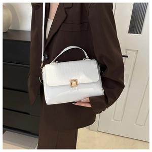Sac bandoulière blanc en cuir croco avec boucle dorée porté sur un costume marron