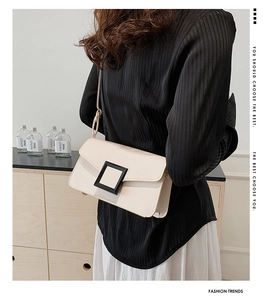 Detail of minimalist cream flap shoulder bag with iconic black buckle decoration