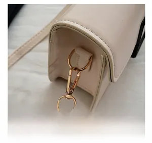 Macro view of gold-toned hardware hook and premium leather strap on an off-white bag