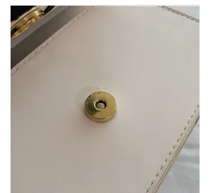 Close-up of golden magnetic snap closure and fine stitching on off-white leather bag