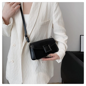 Detail of minimalist black crossbody square bag worn over a white textured blazer