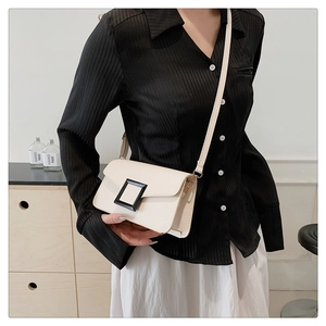 Crossbody view of a cream square bag with a black buckle accent and slim strap