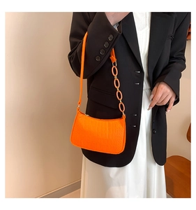 Detail of bright orange faux leather shoulder bag with crocodile pattern and chain link strap