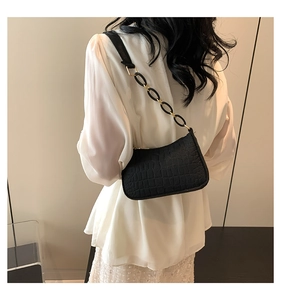 Detail of black crocodile texture baguette bag with golden chain strap on a model