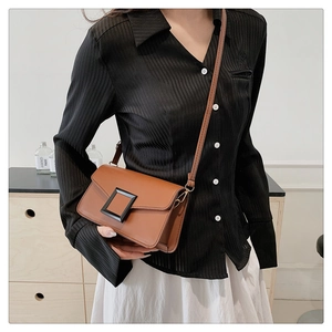 Close-up of a brown leather crossbody bag with a large black resin buckle on a model
