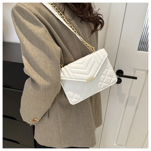 White quilted chain shoulder bag with gold hardware worn by a model in a minimal setting