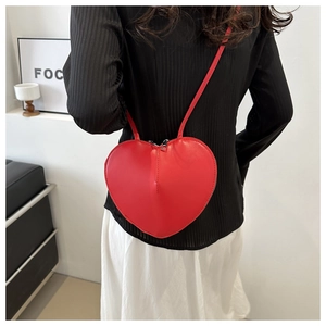 Detail of red heart-shaped leather crossbody bag worn by a model in casual street style