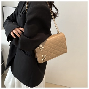 Detail of khaki quilted crossbody bag with golden butterfly hardware worn by a model