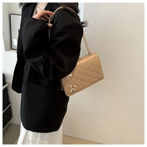 Side view of beige quilted crossbody bag with golden butterfly chain strap on model