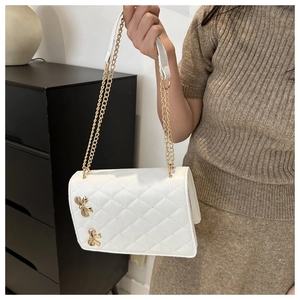 Close-up of white quilted chain bag featuring golden butterfly charms and leather strap