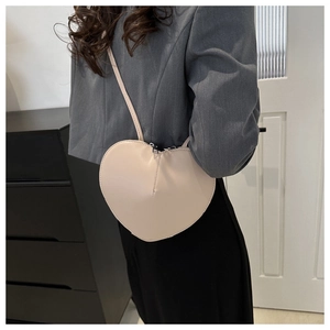 Side view of heart-shaped beige leather crossbody bag worn by model in home setting