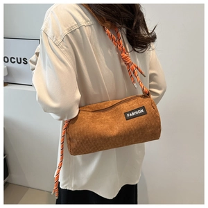 Detail of a brown corduroy cylindrical crossbody bag with woven rope strap and fashion patch