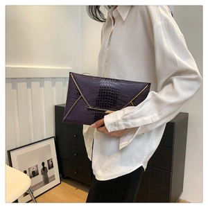 Detail of dark purple crocodile texture envelope clutch bag with gold metal trim