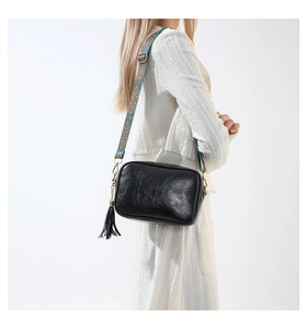 Détail du sac bandoulière vintage noir avec sangle large bleue brodée et pompon