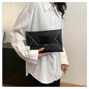 Macro shot of black crocodile-embossed clutch with gold metal accents and trim