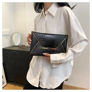 Detail of black envelope clutch featuring gold buckle and crocodile embossed texture