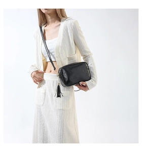 Détail d'un sac à bandoulière noir minimaliste avec pompon à franges et détails métalliques