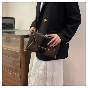 Detail of dark brown croc-embossed envelope clutch with gold V-shape metal trim