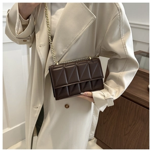 Close-up of deep brown quilted crossbody bag with gold chain strap on stylish trench coat