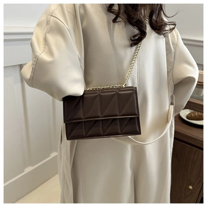 Detail of dark brown geometric quilted crossbody bag with gold chain on white coat