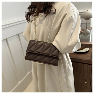 Close-up of dark brown quilted crossbody bag with gold chain strap on beige coat
