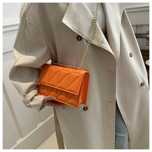 Detail of an orange quilted crossbody bag with gold chain strap on a trench coat