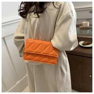 Detail of a bright orange quilted crossbody bag with golden chain strap on a model