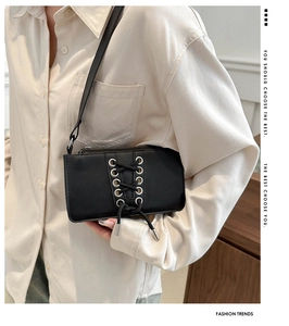 Détail du sac bandoulière en cuir verni noir avec un design de laçage tendance
