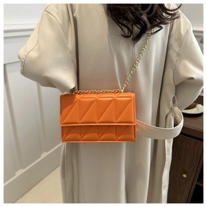 Detail of bright orange quilted crossbody bag with gold chain strap on cream coat