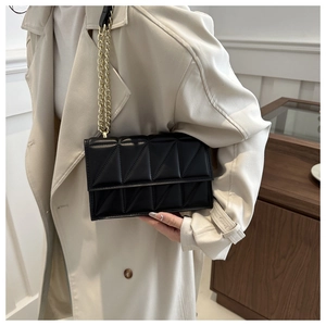 Close-up of black quilted shoulder bag featuring triangle patterns and gold chain strap