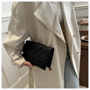 Detail of black quilted leather crossbody bag with triangle pattern and gold chain strap