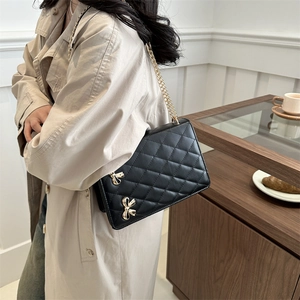 Chic black quilted crossbody bag with golden butterfly chain shown on model in a cafe