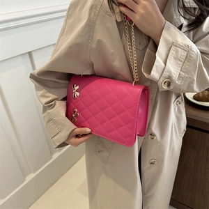 Fuchsia quilted crossbody bag with golden butterfly chain shown on a trench coat