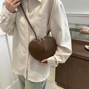 Brown heart-shaped PU leather crossbody bag with dual zippers worn by a female model