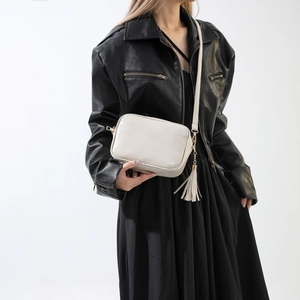 Petit sac carré blanc crème minimaliste avec pompon porté par un mannequin en noir