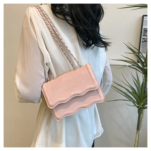 Detail of pink crossbody bag featuring scalloped flap edges and woven metal chain strap