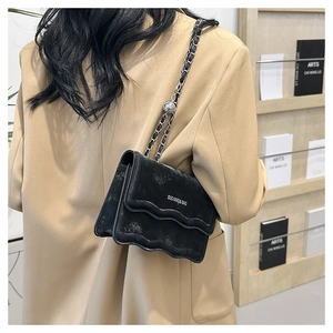 Detail of black crossbody bag with wave edges and silver chain strap on model