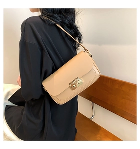 Detail of a beige leather shoulder bag with a gold square lock worn by a model