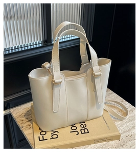 Sac à main en cuir PU blanc crème avec boucles dorées sur une surface en marbre