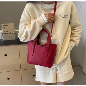 Detail of red leather tote bag with round handles and gold hardware in a modern setting