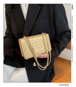 Detail view of stylish gold quilted square bag with metallic chain strap worn by a model