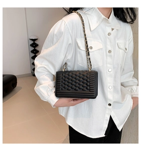 Detail of black bubble quilted crossbody bag with gold chain strap on white shirt
