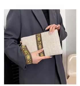 Detail of straw woven clutch with ethnic pattern strap held by a model in gray suit